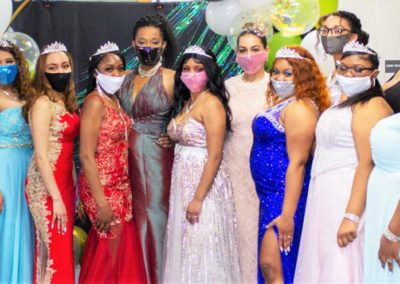 A group of women wearing elegant prom style dresses stand in a row at the event hosted by GEMS.