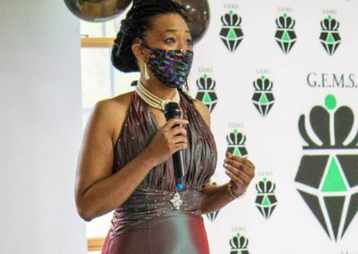 Kenyatta Calloway gives a speech with a microphone while wearing a gown at a GEMS event sponsored by the Gifford Foundation.