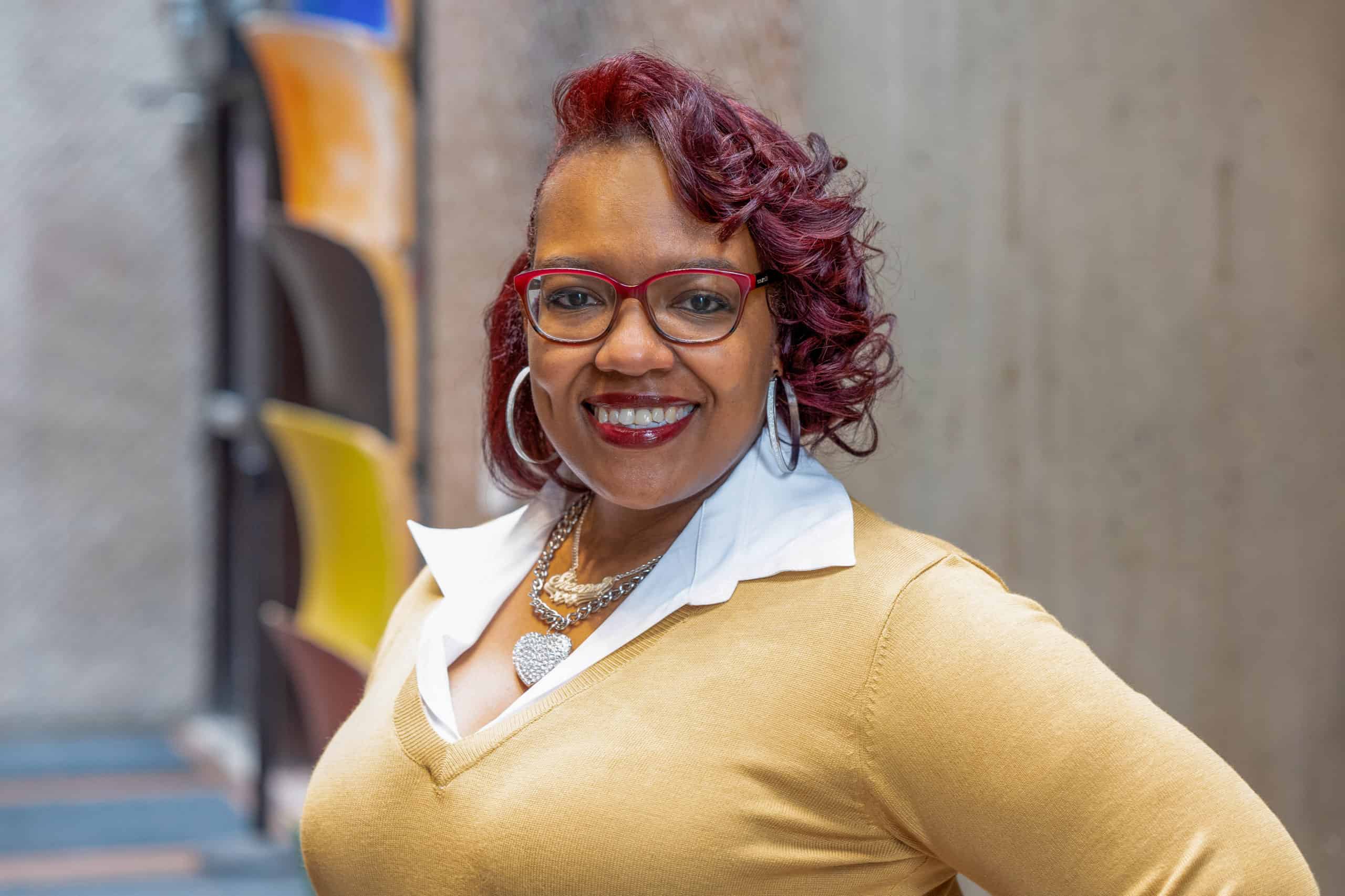 Sheena Solomon is the Executive Director of The Gifford Foundation. She is pictured smiling with a yellow dress and red hair.