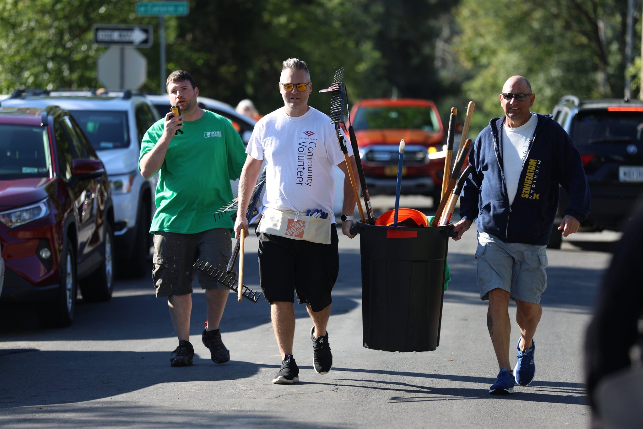 A group of men smile in the sun while carrying a trashcan full of lawn care supplies during the Home HeadQuarters Block Blitz.