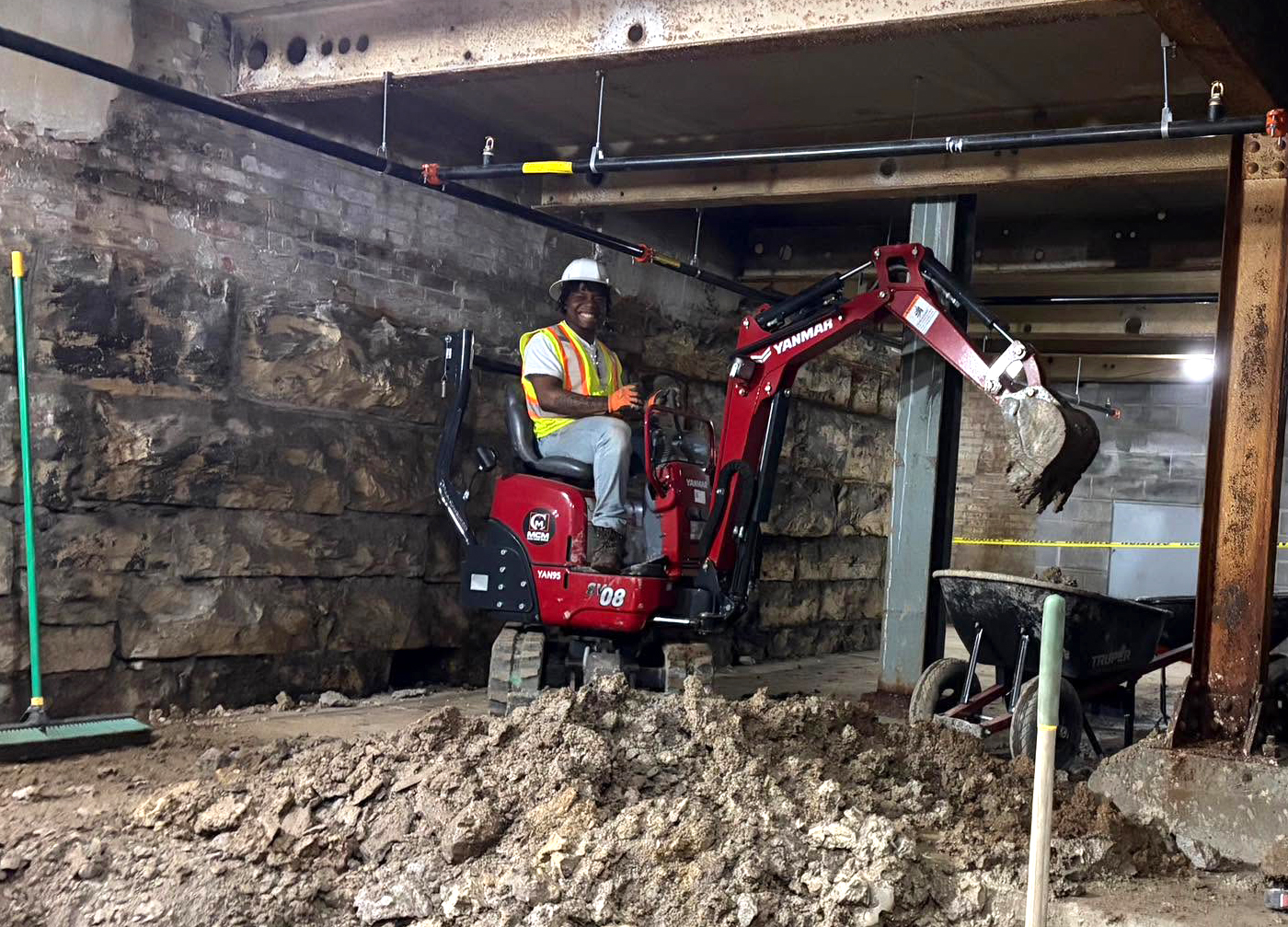 A man operating a small backhoe in a basement of a building that is being constructed