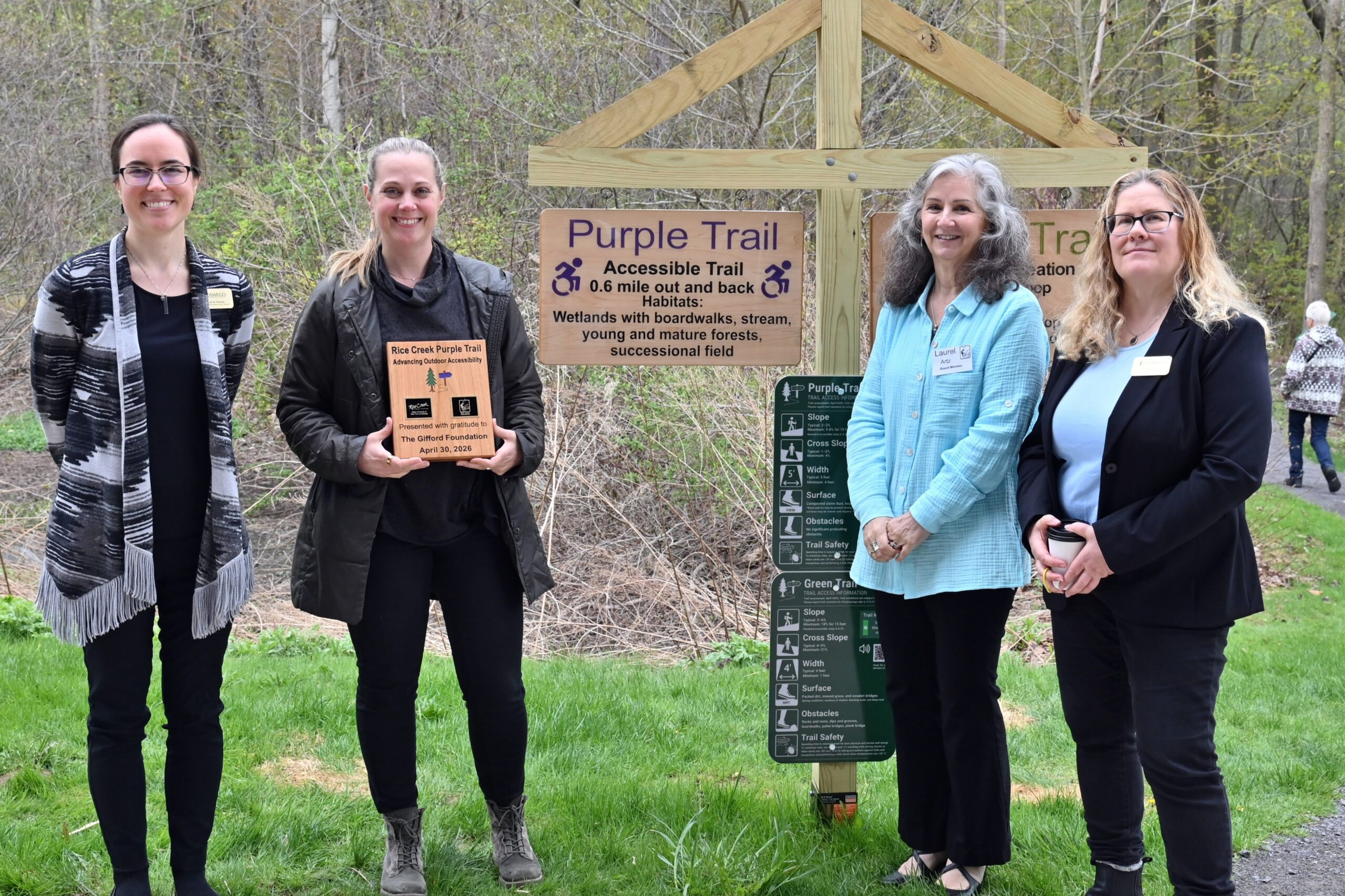 Gifford's Associate Director, Lindsay McClung stands with three other people at a trail head holding a honorary plaque.